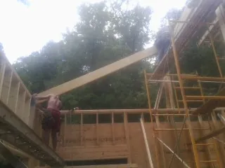 Carpenter raising a rafter beam on a new second story frame in Watertown